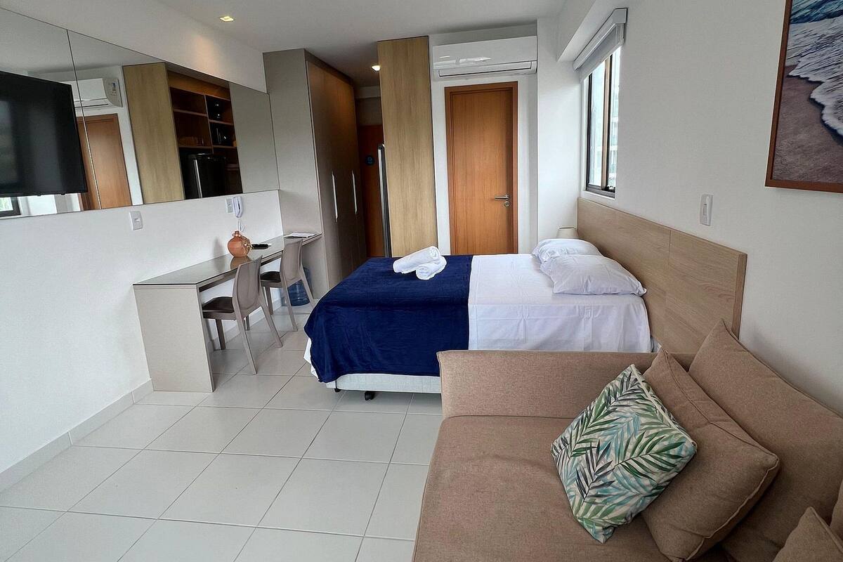 A modern hotel room with a bed, a sofa, a desk, and a TV.