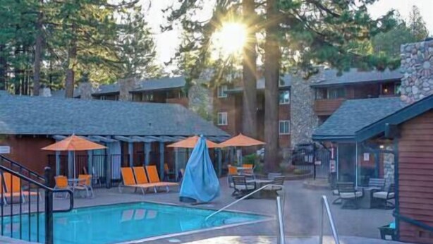 A pool area with lounge chairs and umbrellas, surrounded by buildings with stone facades and a clear sky. - 5 Bedroom, 2 Bath Cabin. 2 Kings, 3 Queens. Full Kitchen, living/dining room. (South Lake Tahoe)