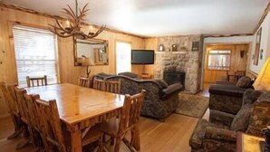 A wooden dining area with a large table and chairs, a stone fireplace, and a television on a stand. - 5 Bedroom, 2 Bath Cabin. 2 Kings, 3 Queens. Full Kitchen, living/dining room. (South Lake Tahoe)