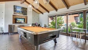 A pool table in a room with wooden flooring, a TV, and a large window with a view of greenery. - 5 Bedroom, 2 Bath Cabin. 2 Kings, 3 Queens. Full Kitchen, living/dining room. (South Lake Tahoe)
