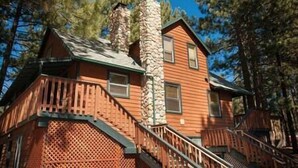 A cabin with a stone chimney, wooden exterior, and a staircase leading to the entrance. - 5 Bedroom, 2 Bath Cabin. 2 Kings, 3 Queens. Full Kitchen, living/dining room. (South Lake Tahoe)