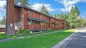 A row of two-story wooden buildings with balconies, surrounded by well-maintained grass and trees.