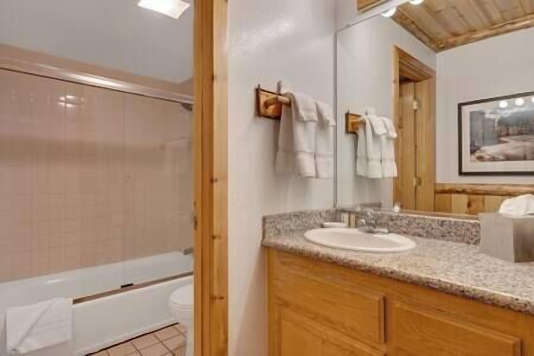A bathroom with a wooden vanity, a sink, and a mirror. There are towels hanging on a rack and a framed picture on the wall.