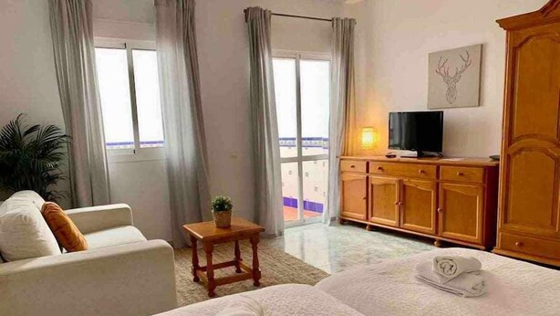 Habitación de hotel con dos camas, un televisor, un armario de madera y un balcón con cortinas.