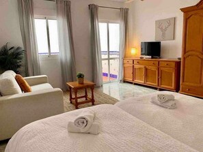 Habitación de hotel con dos camas, un televisor, un armario de madera y un balcón con cortinas.