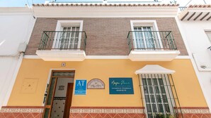 Un edificio de dos pisos con fachada amarilla, un balcón con barandilla de metal y un letrero que indica disponibilidad para alquiler vacacional.