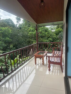 A balcony with a wooden table and bench, a metal railing, and a view of lush greenery.