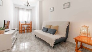 A cozy living room with a sofa, a dining table with chairs, a chandelier, and a small table with a lamp. - Apartment in the center of Nerja with pool (Nerja)