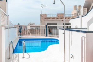 Una piscina en la azotea con barandilla metálica, de color azul cristalino, y vistas de los edificios circundantes.