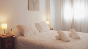 A hotel room with a neatly made bed, two bedside lamps, a wall-mounted artwork of a deer head, and a window with sheer curtains. - Apartment in the center of Nerja with pool (Nerja)