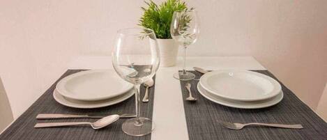 A table set with white plates, two wine glasses, and silver cutlery.