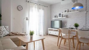 En moderne stue med sofa, sofabord, spisebord, stole, et fjernsyn og en væg med murstensmønster.