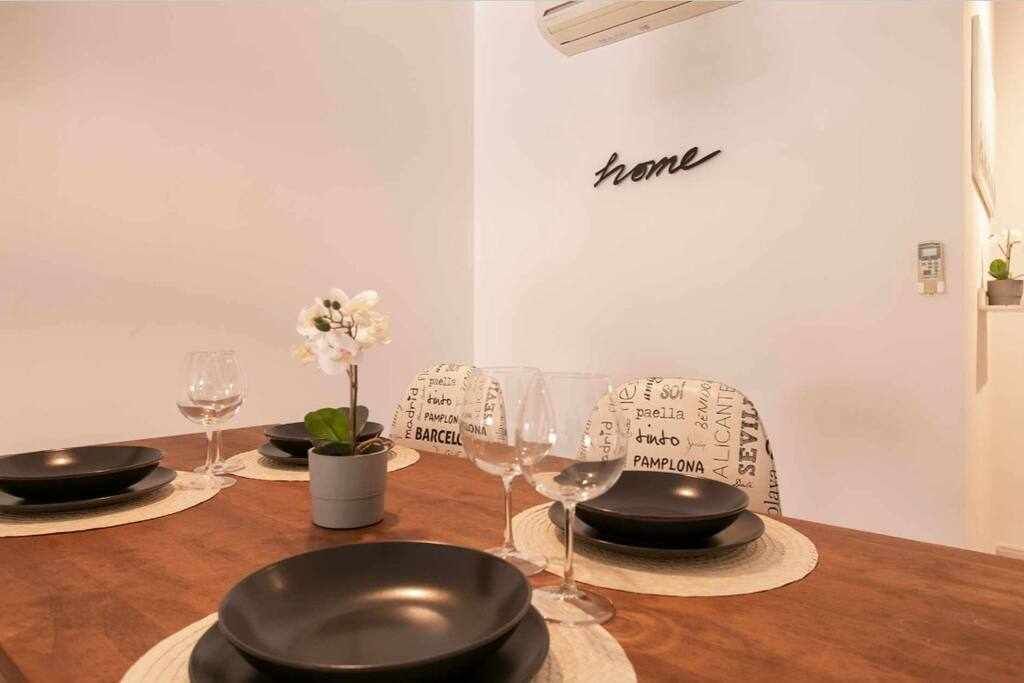Une table à manger dressée avec des assiettes noires, des verres à vin et une petite plante en pot.