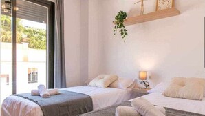A hotel room with two beds, a bedside table with a lamp, and a window with a view of greenery outside. - Modern two bedroom apartment in Nerja center (Nerja)