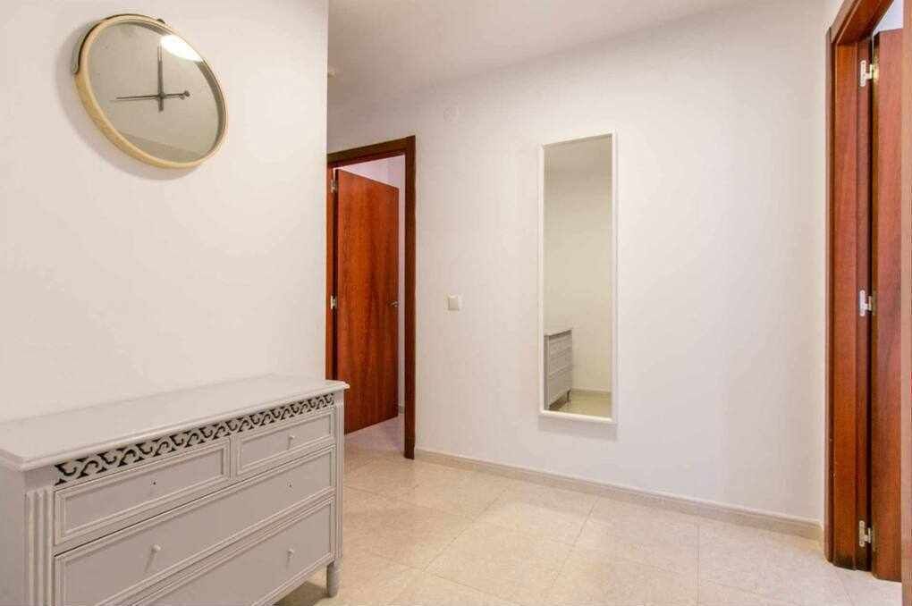Ein Flur mit einer weißen Kommode, einem runden Spiegel und einem rechteckigen Spiegel an der Wand.