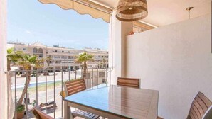 A balcony with a glass table and chairs, overlooking a street with buildings and palm trees. - Modern two bedroom apartment in Nerja center (Nerja)