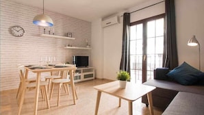 A modern living room with a dining area, a sofa, a TV, and a large window with curtains. - P3. Moderno Apartamento en el Centro de Nerja (Nerja)