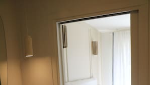 A bedroom with a bed, a white bedside table, a mirror, and a light fixture.