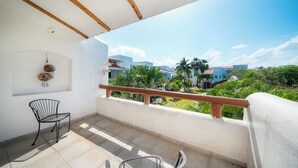 A balcony with two chairs, a view of buildings and greenery, and a white wall with a hanging decoration.