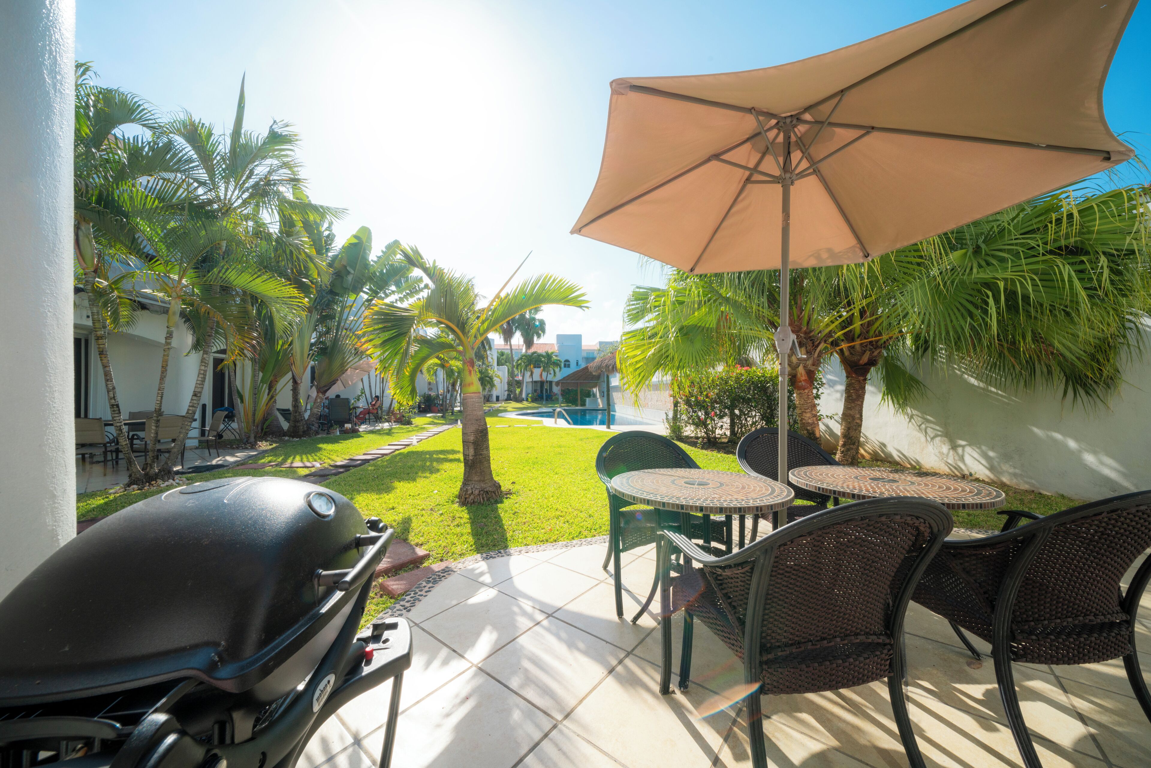 An outdoor patio with a grill, chairs, and an umbrella.