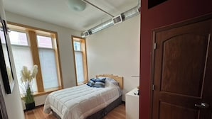 Une chambre à coucher avec un lit, un plancher en bois, une porte et des fenêtres.