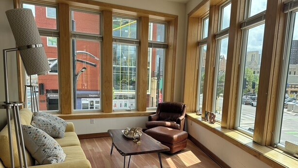 Un salon avec un canapé, une table basse et un fauteuil. De grandes fenêtres offrent une vue sur la rue.