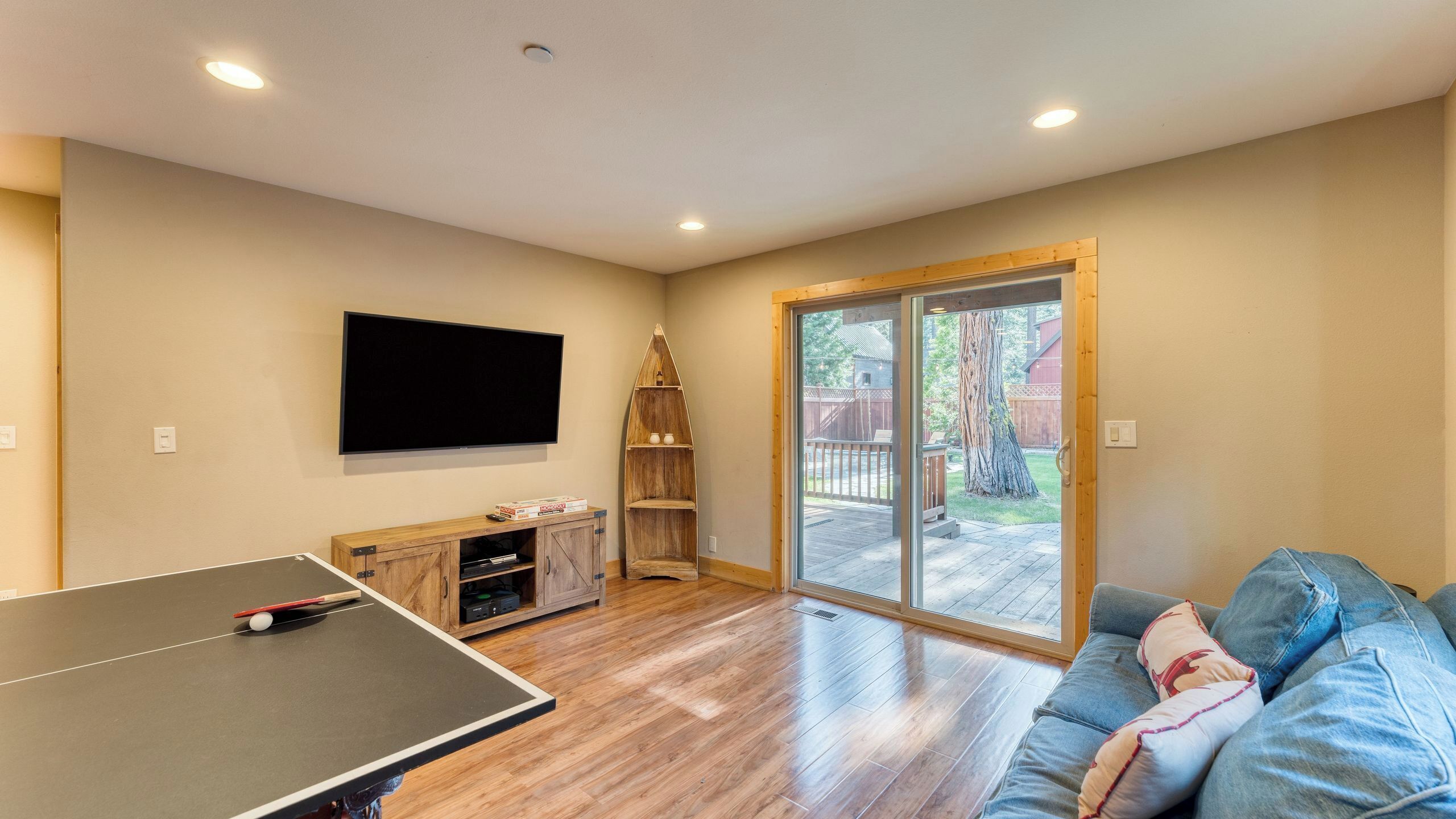 Un salon équipé d’une table de ping-pong, d’un téléviseur à écran plat, d’un meuble en bois et d’une porte-fenêtre coulissante donnant sur une terrasse.