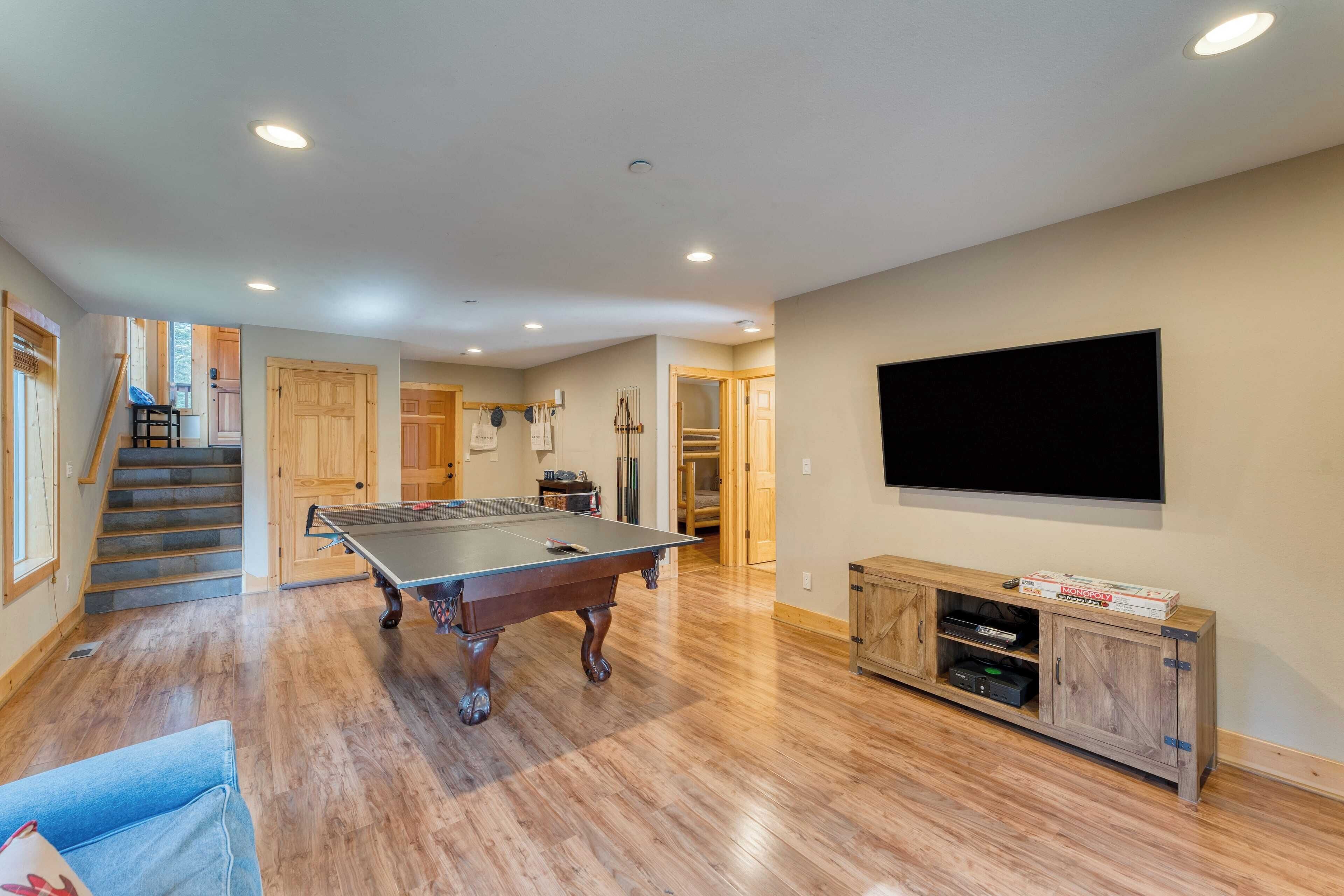 A spacious living room with a ping pong table, wooden flooring, a television, and a wooden cabinet with electronic devices.
