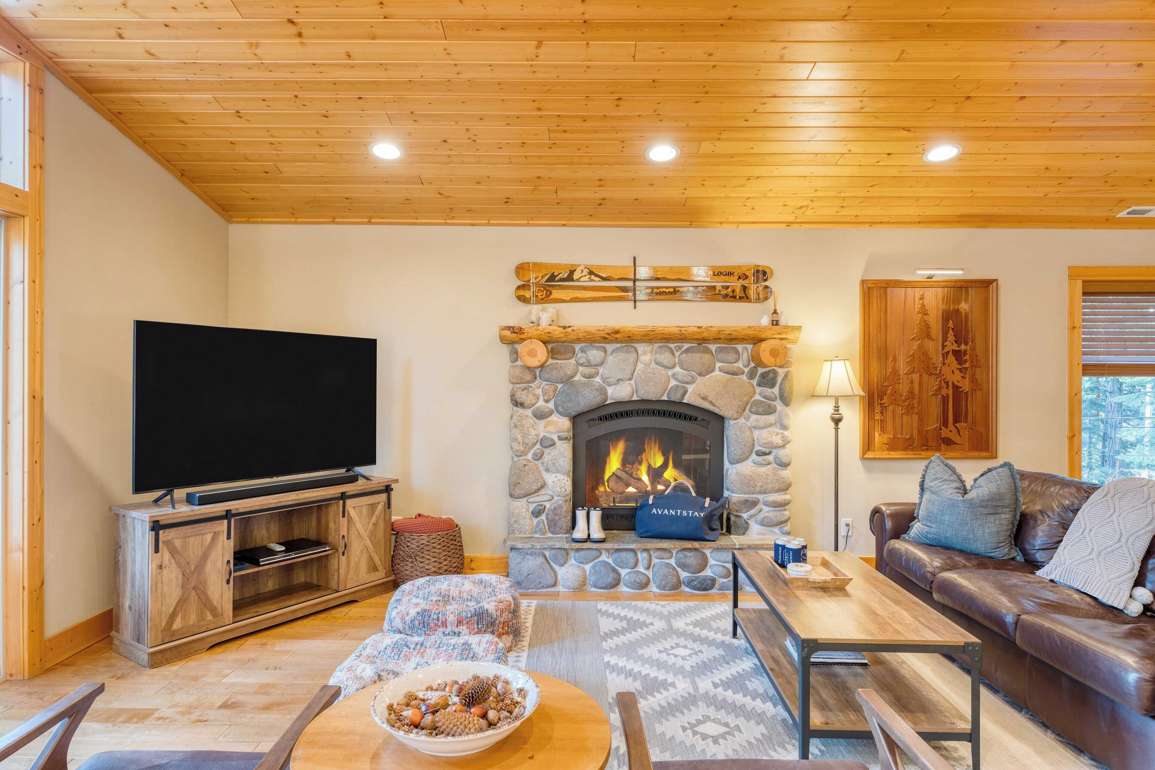 Un salon chaleureux avec une cheminée en pierre, un téléviseur à écran plat, des sièges confortables et un plafond en bois.