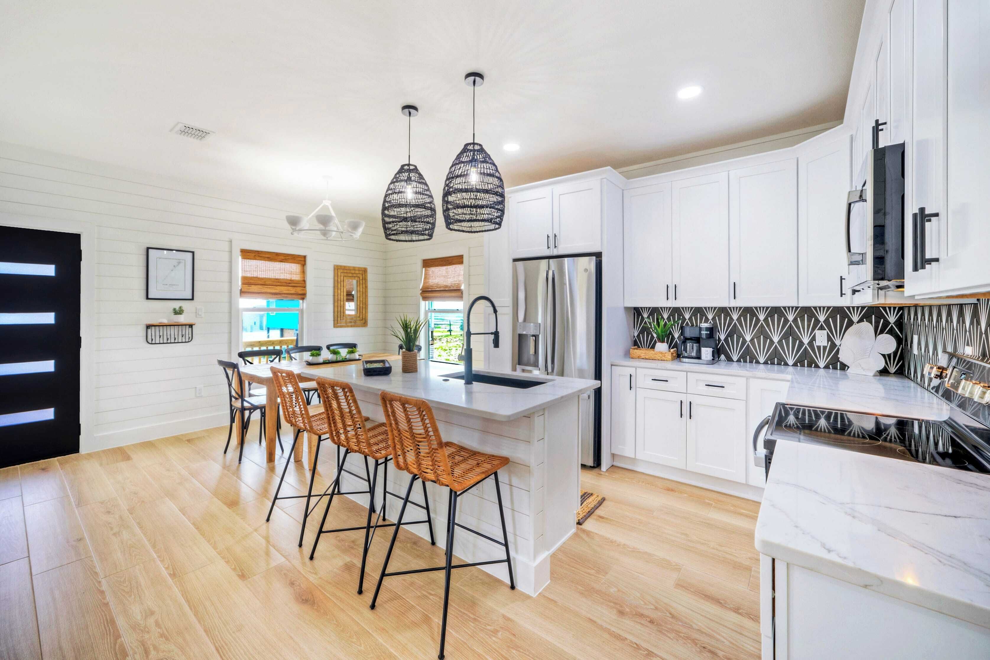A modern kitchen with white cabinetry, a central island with bar stools, pendant lighting, and a stainless steel refrigerator.