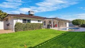 Una casa de dos pisos con piscina, patio cubierto y césped bien cuidado.