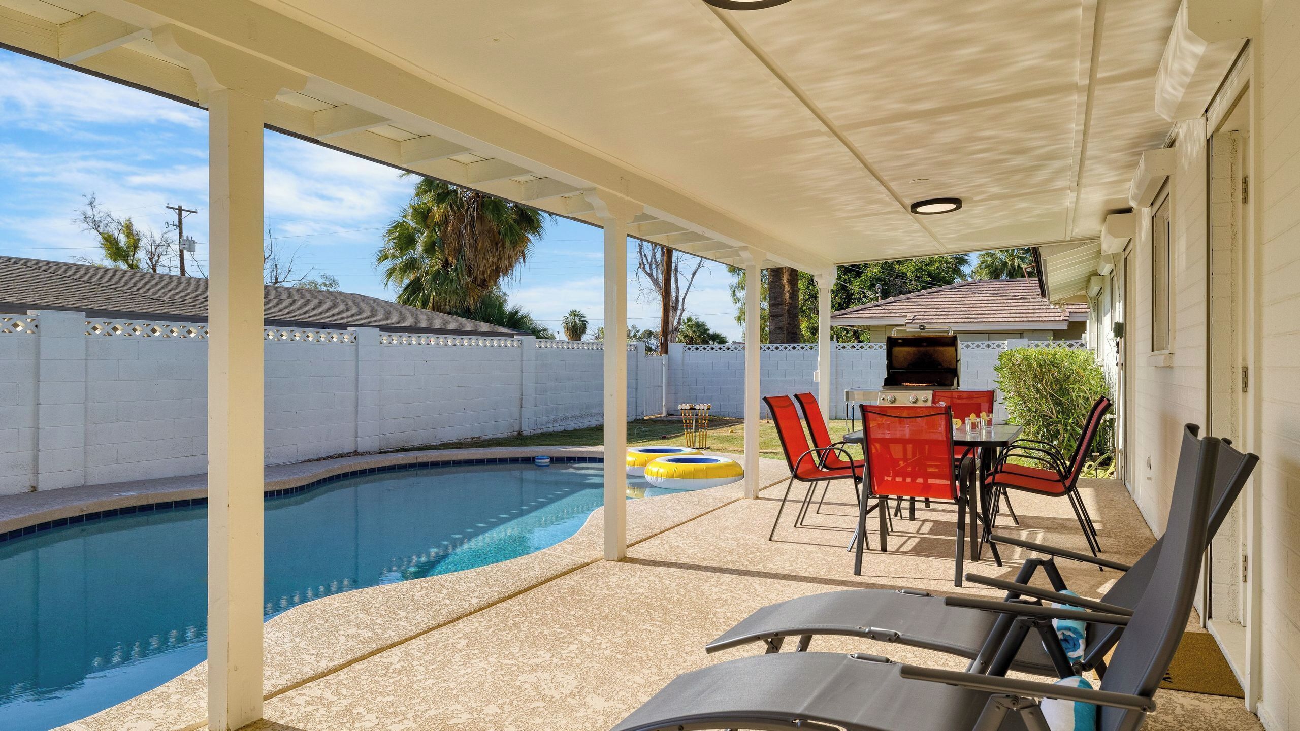 A covered outdoor area with a pool, lounge chairs, and a barbecue grill.
