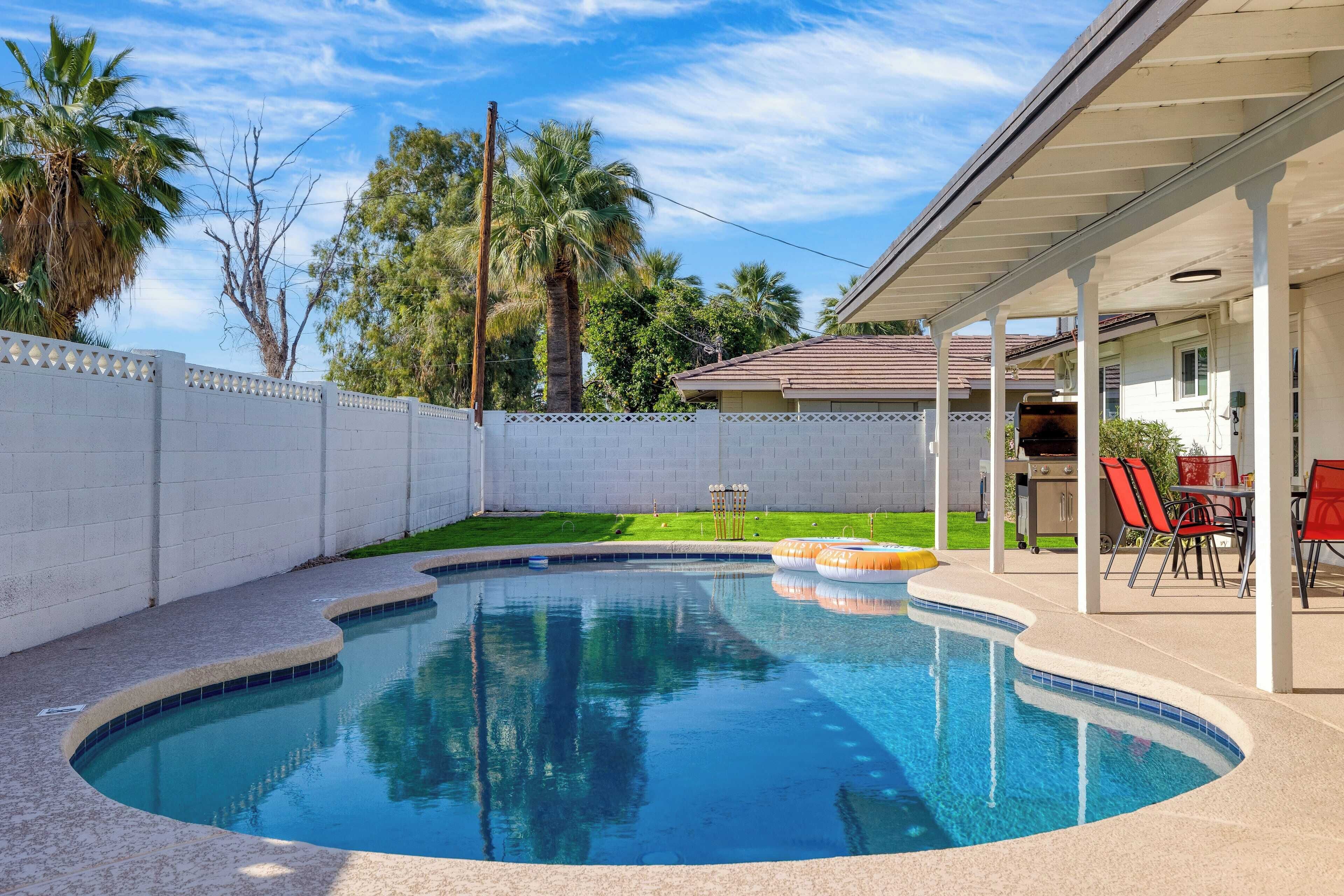 A swimming pool with a curved edge, a covered patio area, and a fenced backyard.