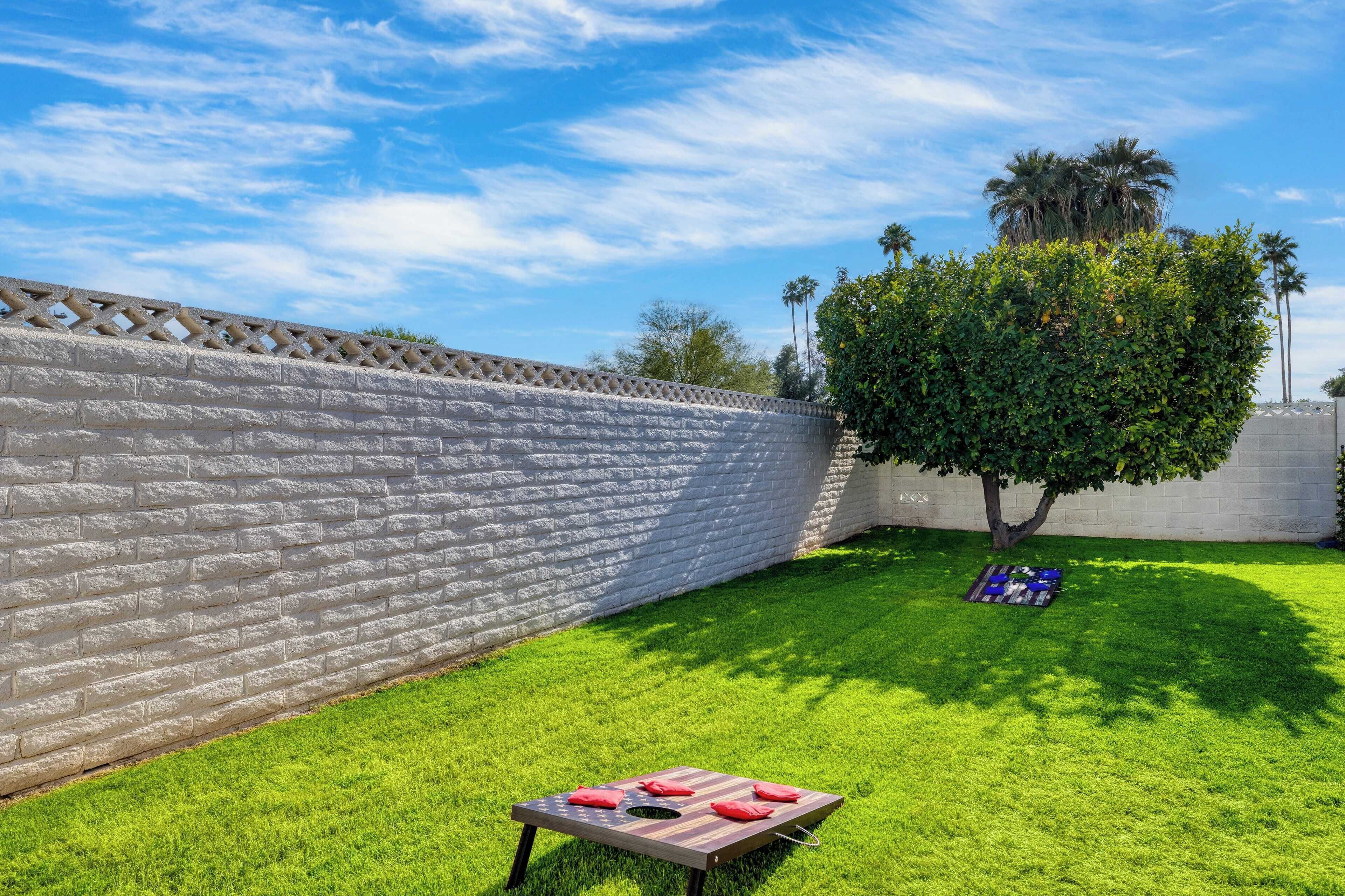 Un jardin bien entretenu, avec un mur en briques, une pelouse soigneusement taillée et une table en bois agrémentée de coussins rouges.