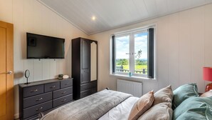 A bedroom with a bed, dresser, TV, window with view, and radiator. - Whitehill Lodge - UK47194 (Walton, near Brampton)