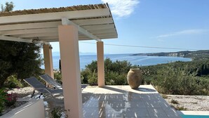 Un espacio exterior techado con piscina, sillones de descanso y vistas al mar.