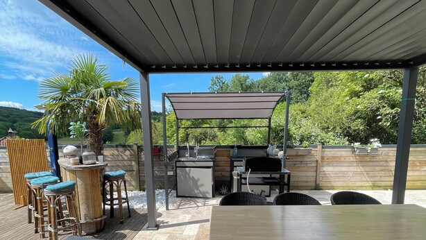 Una terrazza esterna con area salotto coperta, un barbecue e vista sul paesaggio circostante.