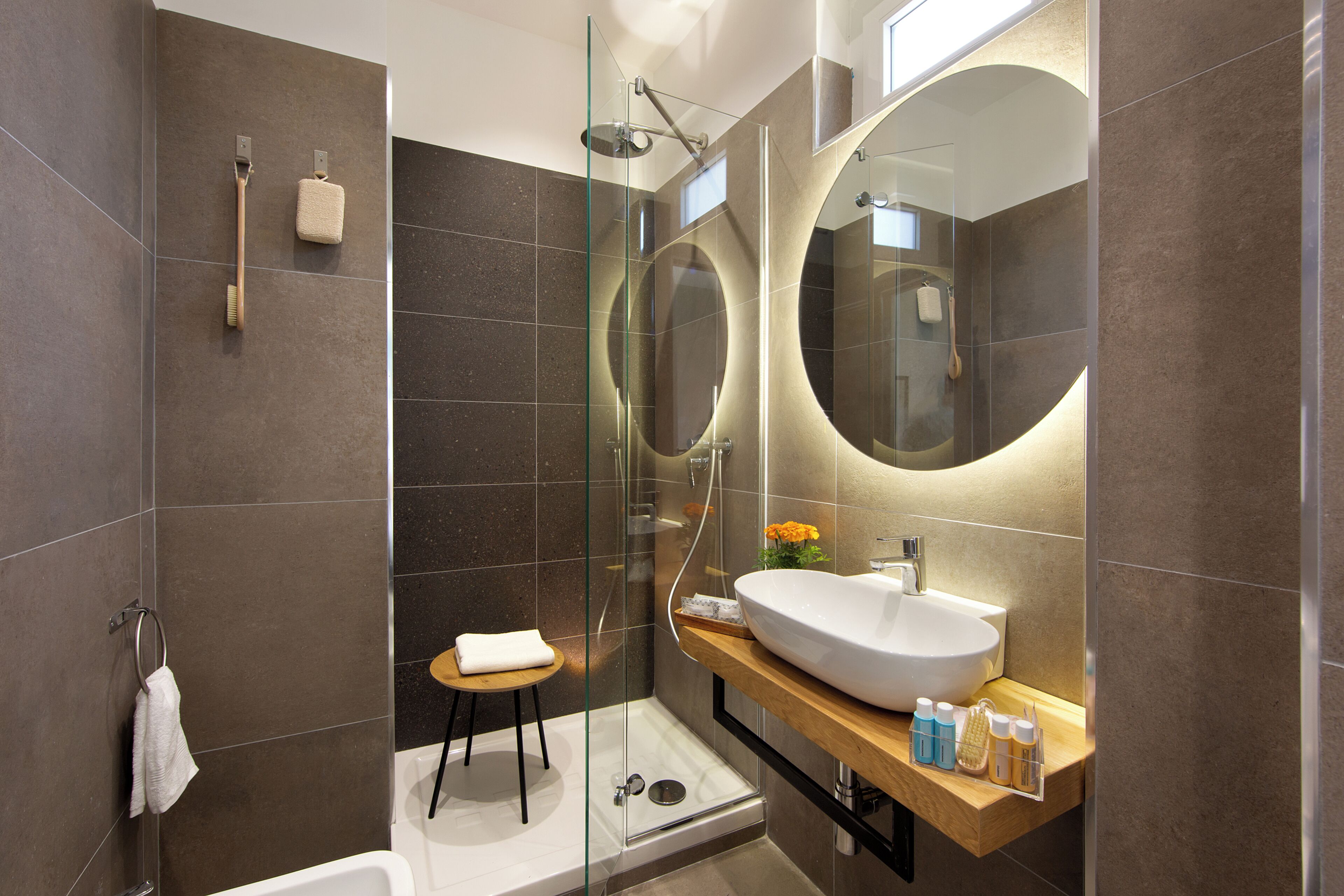 A modern bathroom with a glass-enclosed shower, a large mirror, and a wooden vanity with toiletries.
