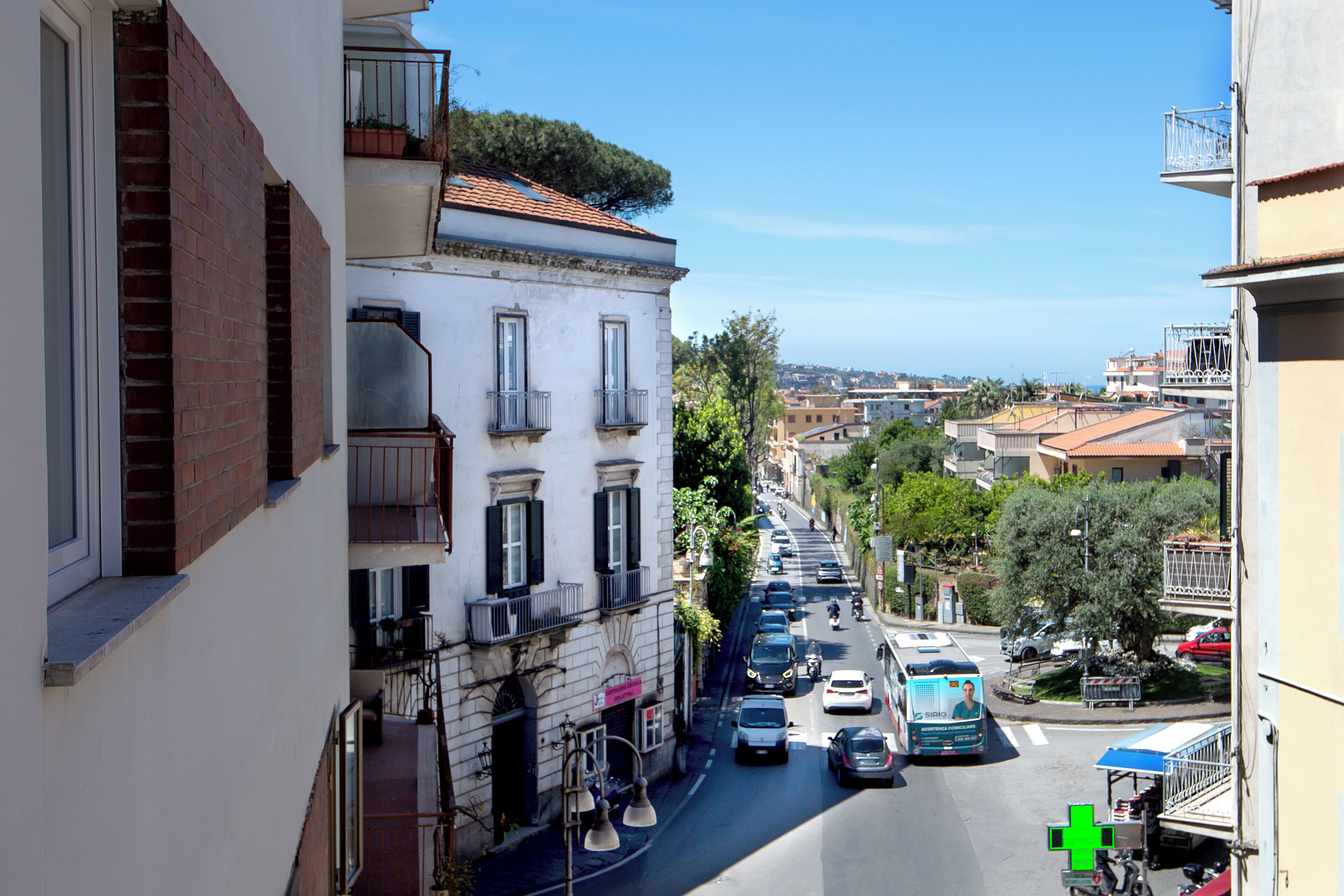 A narrow street with buildings on either side, a clear sky, and a view of the sea in the distance.