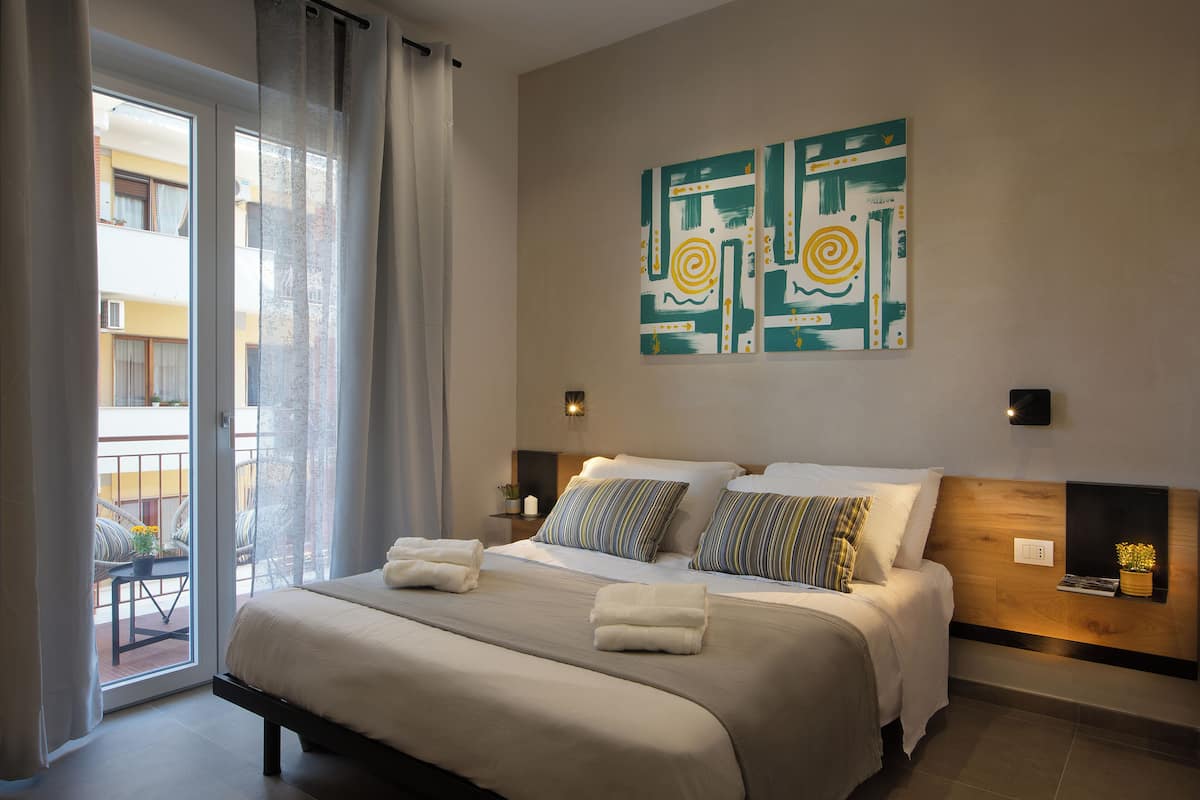 Une chambre d’hôtel avec un grand lit, un balcon offrant une belle vue et une peinture abstraite moderne accrochée au mur.