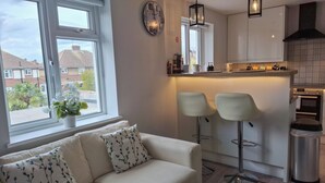 A modern kitchen with two bar stools, a built-in oven, and a window with a view of houses. - NEW 2 bedrooms with private en-suite near Heathrow (Ashford)