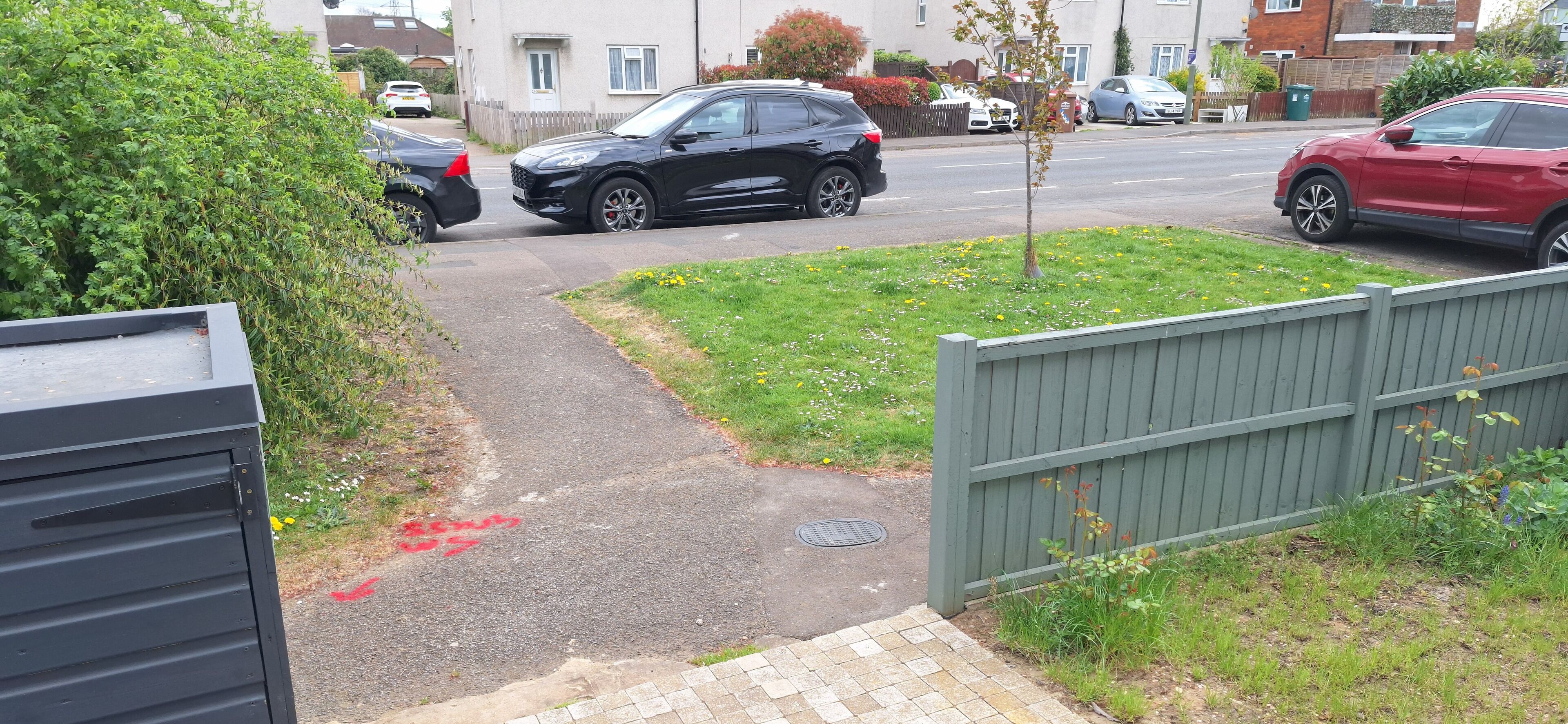 Una calle residencial con casas, una camioneta SUV negra y un auto rojo estacionados al costado.