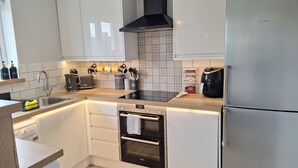 A modern kitchen with white cabinets, a black range hood, a Siemens oven, a coffee maker, and a Siemens refrigerator. - NEW 2 bedrooms with private en-suite near Heathrow (Ashford)