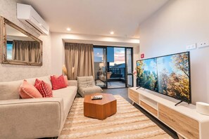 A modern living room with a sofa, coffee table, and a flat-screen TV. - Fitzgerald | 3BR + Parking | Sleeps 7 (Christchurch)