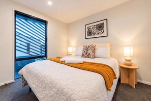 Una camera d'albergo con un letto grande, una finestra con tende, un'opera d'arte appesa al muro, due lampade da comodino e un pavimento con moquette.