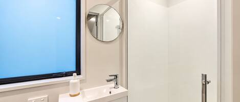 A modern bathroom with a window, a sink, a mirror, and a shower.