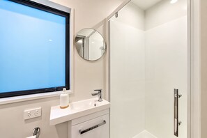 A modern bathroom with a window, a sink, a mirror, and a shower. - Fitzgerald | 3BR + Parking | Sleeps 7 (Christchurch)