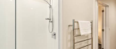 A modern bathroom with a glass shower enclosure, a towel rack with a folded towel, and a door leading to another room.