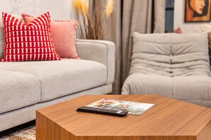 Un soggiorno con un divano grigio, un tavolino in legno con un telecomando e cuscini decorativi.