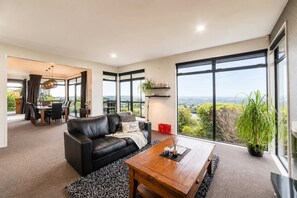 A modern living room with a leather sofa, a wooden coffee table, and a large window offering a city view. - City Views | 4BR | Sleeps 10 | Christchurch (Christchurch)
